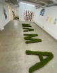 Eine Raumansicht der Ausstellnung mit den ausgeschnittenen Buchstaben MAMA, die aus Erde mit Gras bestehen